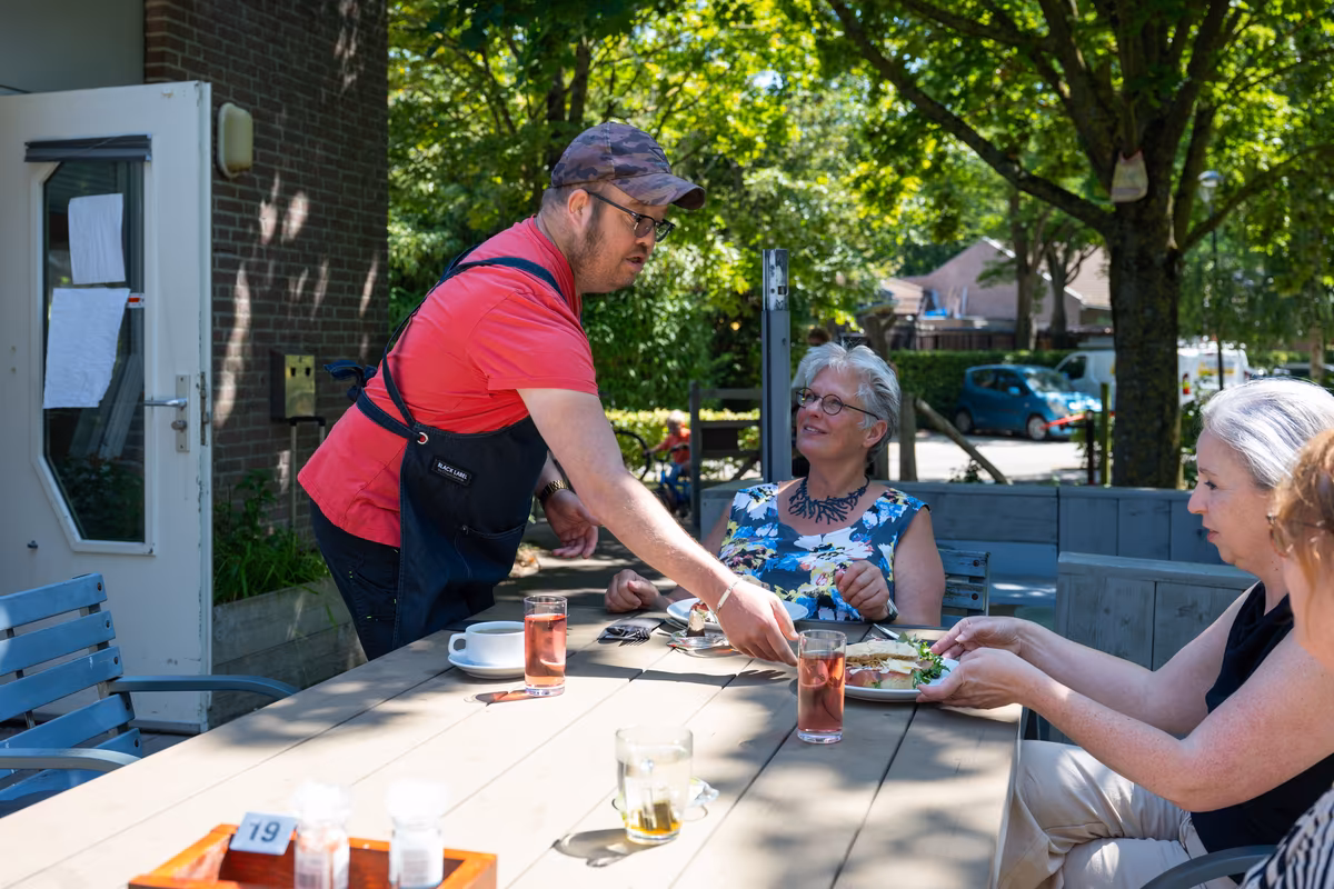 Bediening op het terras Cliënt serveert een gerecht aan gasten op het terras van De Waterjuffers