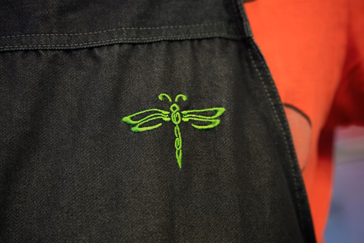 Logo van De Waterjuffers Groen waterjufferlogo geborduurd op een zwart schort